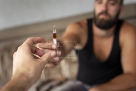 Foto de Detalle de dos manos de usuario de drogas intravenosas compartiendo una jeringa de heroína; drogadictos disparando con heroína. Enfoque selectivo en el jarabe y los dedos que lo sostienen - Imagen libre de derechos