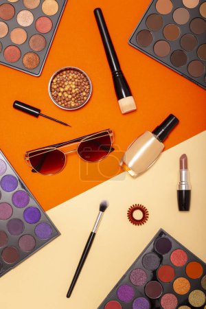 Foto de Disposición plana de varios productos de maquillaje sobre un fondo colorido. Maquillaje de pinceles, coloretes, polvos faciales, lápiz labial, delineador de ojos y gafas de sol - Imagen libre de derechos