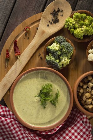 Photo for Table top shot of fresh creamy broccoli soup with some fresh vegetables, spices and croutons next to it. Focus on the dill leaves - Royalty Free Image