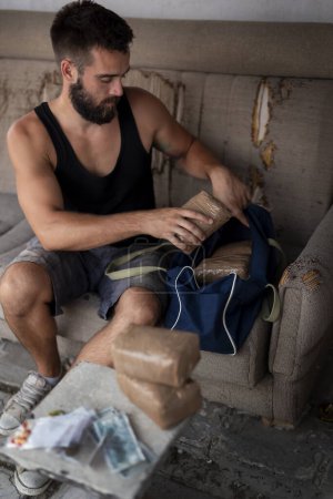 Foto de Traficante de drogas preparando mercancías para el tráfico, embalaje de ladrillos de cocaína, pastillas y marihuana en una bolsa de lona - Imagen libre de derechos