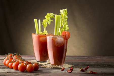Foto de Cóctel Bloody Mary con vodka, jugo de limón y tomate, salsa de tabasco y cubitos de hielo decorados con hojas de apio. Enfoque selectivo en el vidrio adecuado - Imagen libre de derechos