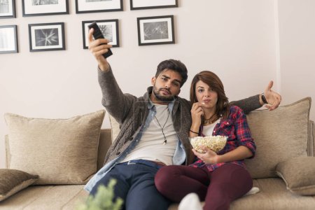 Téléchargez les photos : Couple amoureux assis sur un canapé du salon, regarder un match à la télévision et manger du pop-corn, agacé à cause de la perte de leurs équipes - en image libre de droit