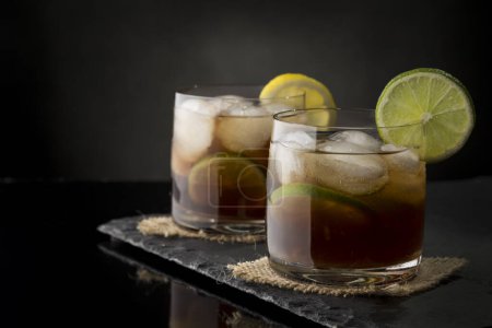 Téléchargez les photos : Cuba cocktails Libre au rhum brun, jus de citron, coke et glaçons, décorés de tranches de lime fraîche sur un plateau moderne en pierre noire - en image libre de droit