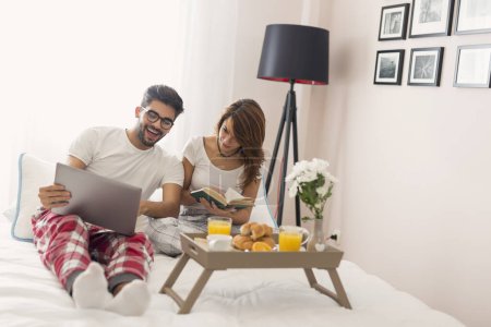 Photo for Beautiful young couple in love having fun reading and surfing the net while having breakfast in bed - Royalty Free Image