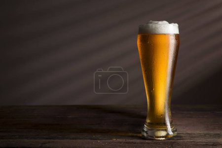 Foto de Vaso de cerveza fría y pálida colocado sobre una mesa rústica de madera - Imagen libre de derechos