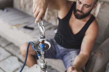 Photo for Man placing hot charcoal on top of a hookah flavored tobacco - Royalty Free Image