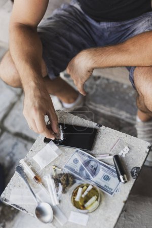 Foto de Detalle de manos masculinas cortando la línea de heroína con una cuchilla de afeitar en una pantalla de teléfono inteligente, preparándola para su uso - Imagen libre de derechos