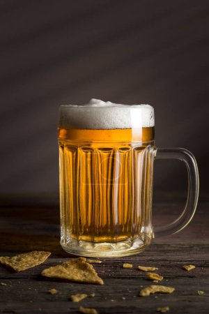 Téléchargez les photos : Tasse de bière froide pâle avec des chips de tortilla sur une table en bois rustique - en image libre de droit