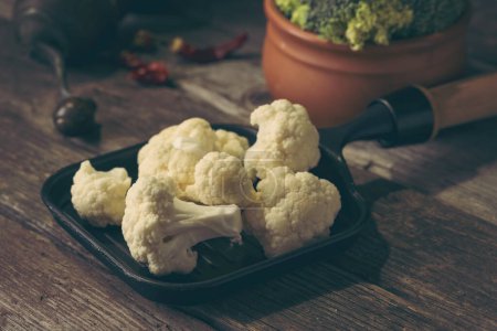 Photo for Fresh pieces of cauliflower and broccoli in small frying pan and rustic clay bowl. Selective focus on the cauliflower - Royalty Free Image