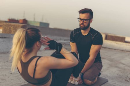 Photo for Beautiful young couple working out on a building rooftop terrace, woman doing crunches - Royalty Free Image