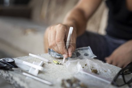 Photo for Detail of male hands rolling a joint with rolling paper and cannabis buds in the foreground. Focus on the tip of the fingers and the joint - Royalty Free Image