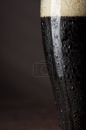Foto de Primer plano de un vaso húmedo de cerveza fría oscura con espuma. - Imagen libre de derechos