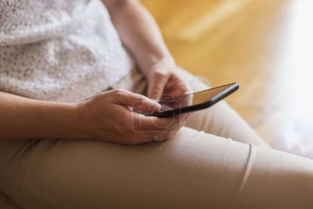 Téléchargez les photos : Détail des mains féminines tenant un téléphone intelligent et lisant un ebook pendant la campagne de pandémie de coronavirus rester à la maison - en image libre de droit
