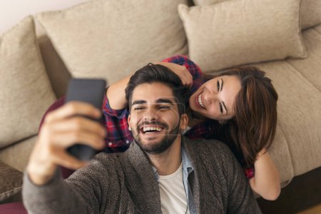Téléchargez les photos : Couple amoureux profiter de leur temps libre à la maison, faire des visages et prendre des selfies. Concentrez-vous sur le gars - en image libre de droit