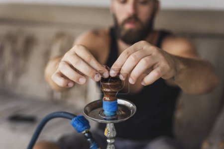 Photo for Man filling up the hookah with fruity flavored, molasses based eastern tobacco, getting it ready for use - Royalty Free Image