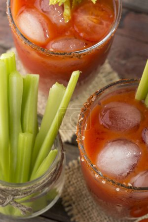 Foto de Vista de ángulo alto de un cóctel Bloody Mary con vodka, jugo de limón y tomate, salsa de tabasco y cubitos de hielo decorados con hojas de apio. Enfoque selectivo - Imagen libre de derechos