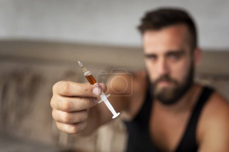 Foto de Consumidor de heroína intravenosa que ofrece heroína inyectable a otra persona; drogadicto que sostiene una jeringa de heroína. Enfoque en la aguja y la jeringa - Imagen libre de derechos