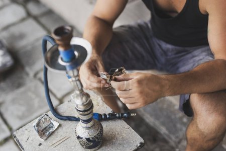 Man filling up the hookah with fruity flavored, molasses based eastern tobacco, getting it ready for use. Focus on the fingers and the tobacco
