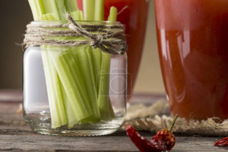 Photo for Bloody Mary cocktail with vodka, lemon and tomato juice, tabasco sauce and ice cubes decorated with celery leaves. Focus on the jar with celery leaves - Royalty Free Image