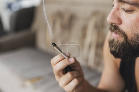 Photo for Young man sitting on a couch, relaxing and smoking pot - Royalty Free Image