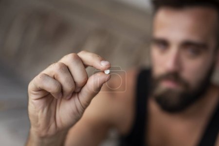 Téléchargez les photos : Un homme tenant une pilule d'ecstasy. Focus sur la pilule - en image libre de droit