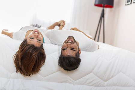 Téléchargez les photos : Couple s'amusant couché au lit et suspendu à l'envers le matin après s'être réveillé - en image libre de droit
