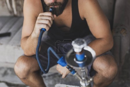 Photo for Man inhaling fruity flavored, molasses based tobacco using a water pipe or hookah. Focus on the mouth - Royalty Free Image