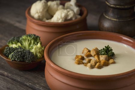 Photo for Cauliflower cream soup decorated with some croutons on a rustic wooden table. Selective focus on the croutons - Royalty Free Image
