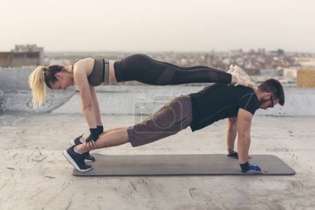 Téléchargez les photos : Couple s'entraînant sur un toit-terrasse du bâtiment, faisant un exercice de planche à bras droit - en image libre de droit