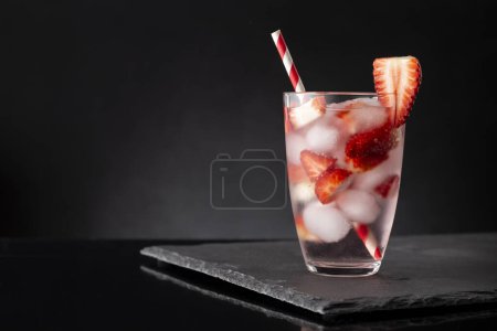 Photo for Glass of cold infused water with fresh strawberry slices on a black stone tray - Royalty Free Image