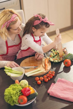 Photo for Mother and daughter cutting vegetables and making salad. Focus on the daughter - Royalty Free Image