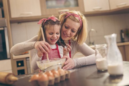 Téléchargez les photos : Belle petite fille aidant sa mère dans la cuisine pour pétrir une pâte à pizza - en image libre de droit