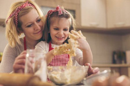 Foto de Hermosa chica amasando masa con su madre en una cocina - Imagen libre de derechos