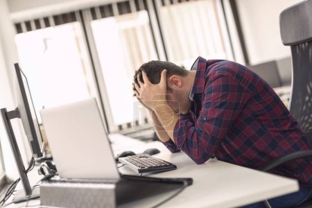 Téléchargez les photos : Jeune développeur de logiciels assis à son bureau au travail, tête dans les mains, stressé en raison d'une défaillance et d'un dysfonctionnement du code - en image libre de droit