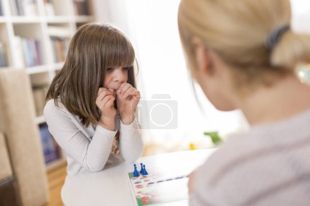 Photo for Mother and daughter sitting in a playroom, playing a ludo game - Royalty Free Image