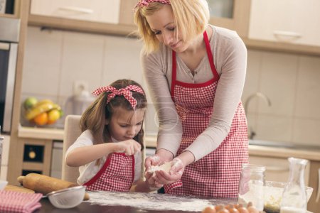 Photo for Little girl sprinkling flour over the kitchen table, helping her mother to bake a pizza dough. Focus on the daughter - Royalty Free Image