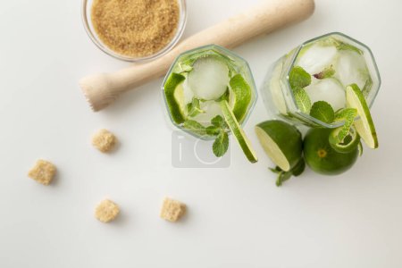 Photo for Top view of two mojito cocktails with lots of ice, white rum, lemon juice and tonic, decorated with lime slices and mint leaves on a modern white table - Royalty Free Image
