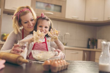 Photo for Beautiful girl kneading dough with her mother in a kitchen. Focus on the daughter - Royalty Free Image
