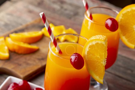 Photo for High angle view of two cold tequila sunrise cocktails with tequila, pomegranate juice and orange juice decorated with slices of orange and maraschino cherries. Selective focus on the cherry - Royalty Free Image