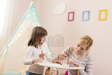 Photo for Mother and daughter playing in a play room, drawing with crayons. Focus on the daughter - Royalty Free Image
