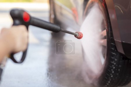Téléchargez les photos : Détail des mains féminines lavant des pneus de voiture avec de l'eau chaude à haute pression et du détergent - en image libre de droit
