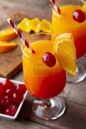 Foto de Vista de ángulo alto de dos cócteles de salida del sol de tequila fría con tequila, jugo de granada y jugo de naranja decorado con rodajas de cerezas de naranja y maraschino. Concéntrate en la cereza en el vaso - Imagen libre de derechos