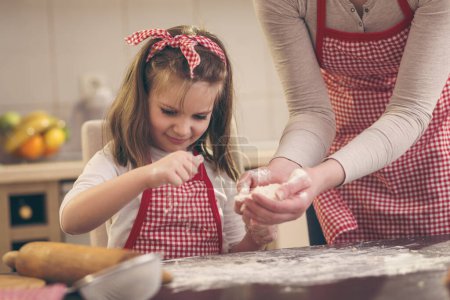 Foto de Niña rociando harina sobre la mesa de la cocina, ayudando a su madre a hornear una masa de pizza - Imagen libre de derechos