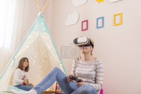 Téléchargez les photos : Mère et fille assises sur le sol dans une salle de jeux, jouant à des jeux vidéo et s'amusant - en image libre de droit