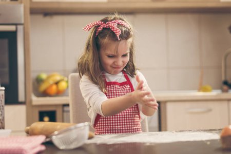 Téléchargez les photos : Petite fille joyeuse jouant dans la cuisine, cuisinant des biscuits et jouant avec de la farine - en image libre de droit