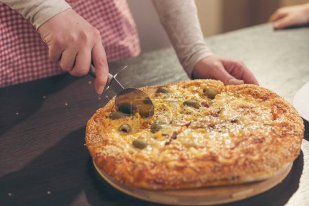 Photo for Detail of female hand cutting pizza with pizza cutter. Selective focus on the knife and pizza - Royalty Free Image