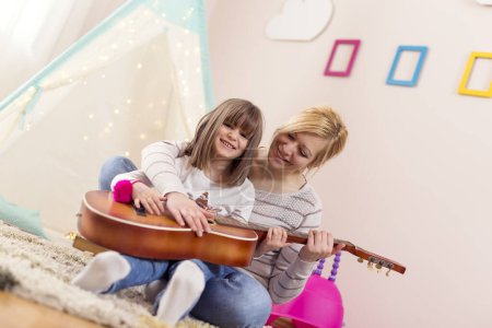 Foto de Alegre madre e hija sentadas en el piso de la sala de juegos, tocando la guitarra y cantando - Imagen libre de derechos