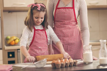 Foto de Madre e hija horneando galletas en la cocina; niña usando un rodillo, amasando masa de galletas - Imagen libre de derechos