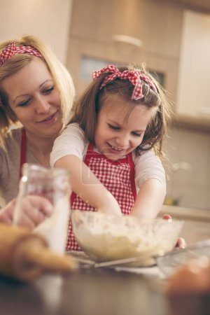 Foto de Hermosa niña ayudando a su madre en la cocina a amasar una masa de pizza. Concéntrate en la hija - Imagen libre de derechos