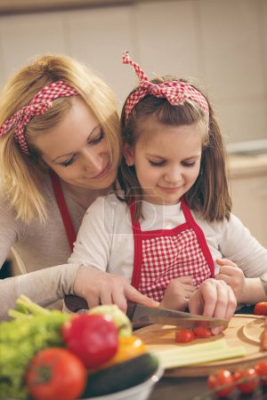 Photo for Mother and daughter cutting vegetables and making salad. Focus on the mother - Royalty Free Image